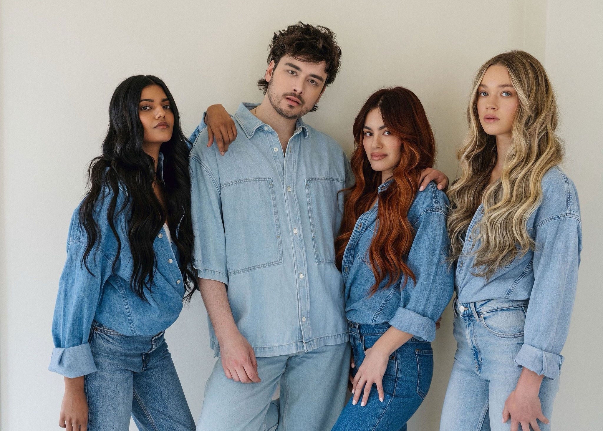 Four people wearing matching blue denim outfits against a white background